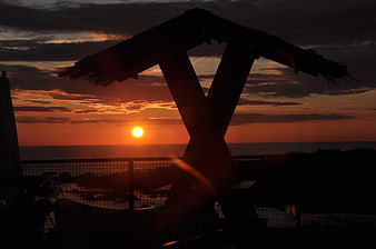 Silhouette of wooden structure against vibrant sunset over ocean