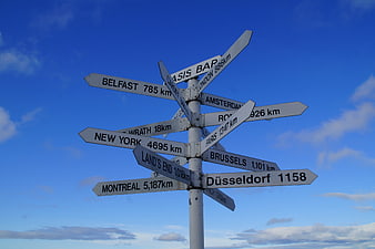 White Directional Signpost With City Names Against Blue Sky