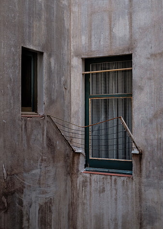 Weathered concrete wall with two windows and wire mesh