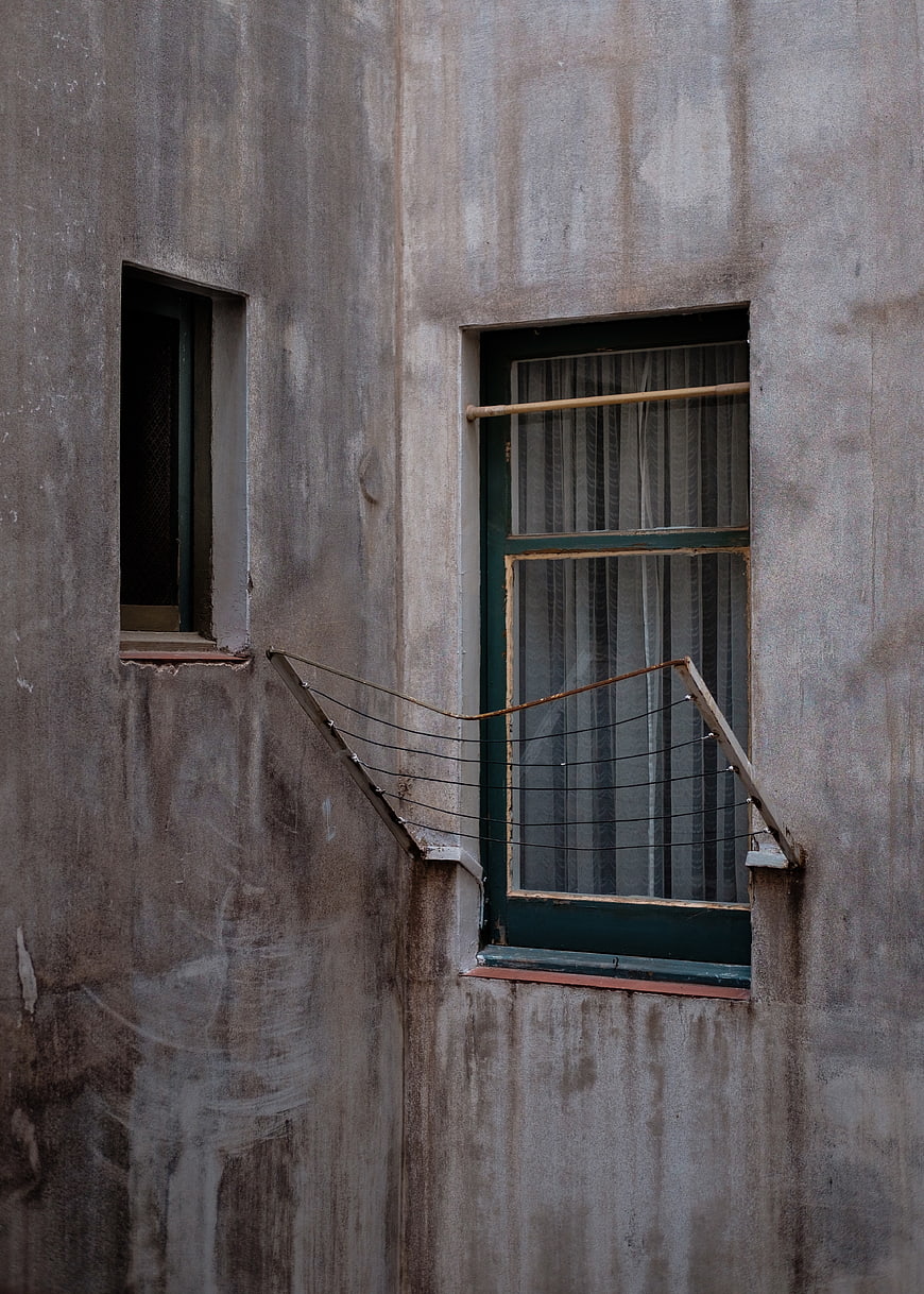 Weathered concrete wall with two windows and wire mesh