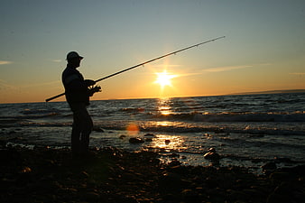 Silhouette of Man Fishing on Rocky Beach at Sunset