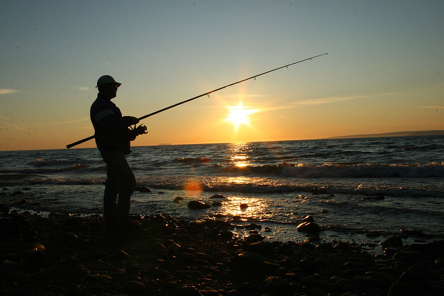 Silhouette of Man Fishing on Rocky Beach at Sunset