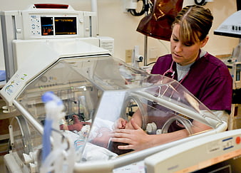 Nurse caring for newborn baby in hospital incubator