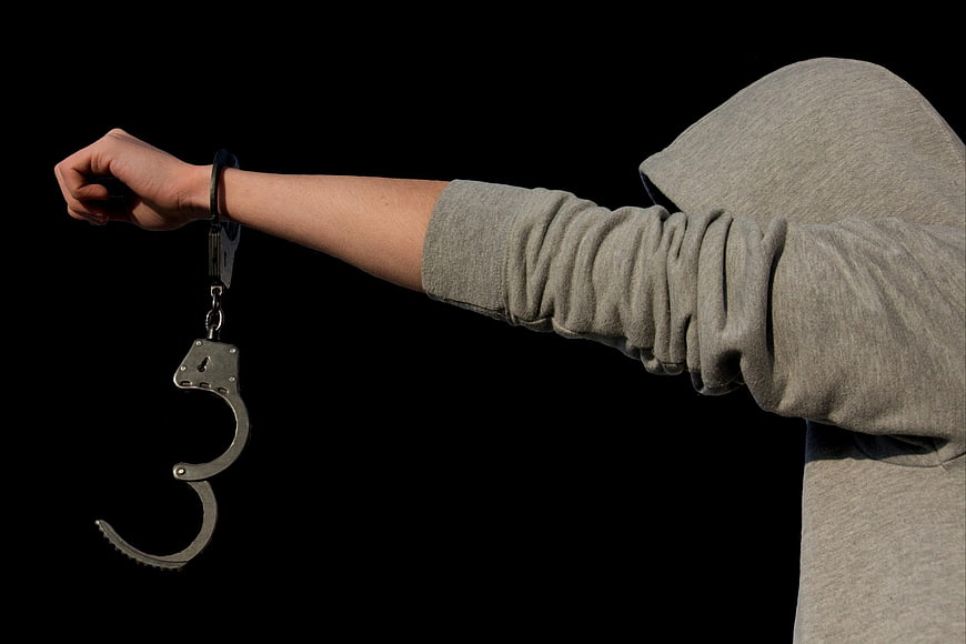 Anonymous hooded figure with dangling handcuffs on black background