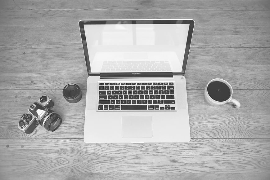 Black and white flat lay of laptop, vintage camera, and coffee