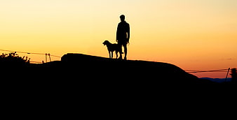 Silhouette of Man and Dog Standing on Hill at Sunset