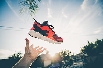 Red and black sneaker tossed in the air against a sunny sky