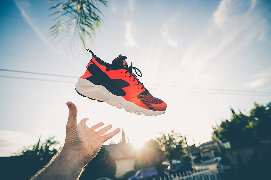 Red and black sneaker tossed in the air against a sunny sky