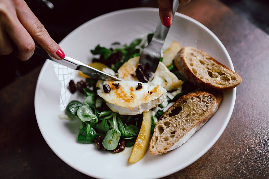 Hands cutting grilled goat cheese salad with bread