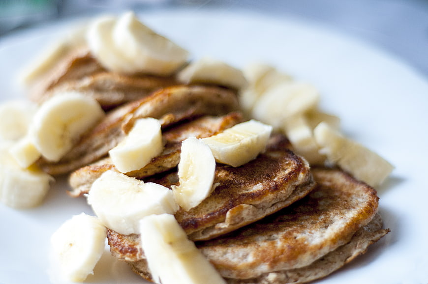 Stack of pancakes with sliced bananas on a white plate