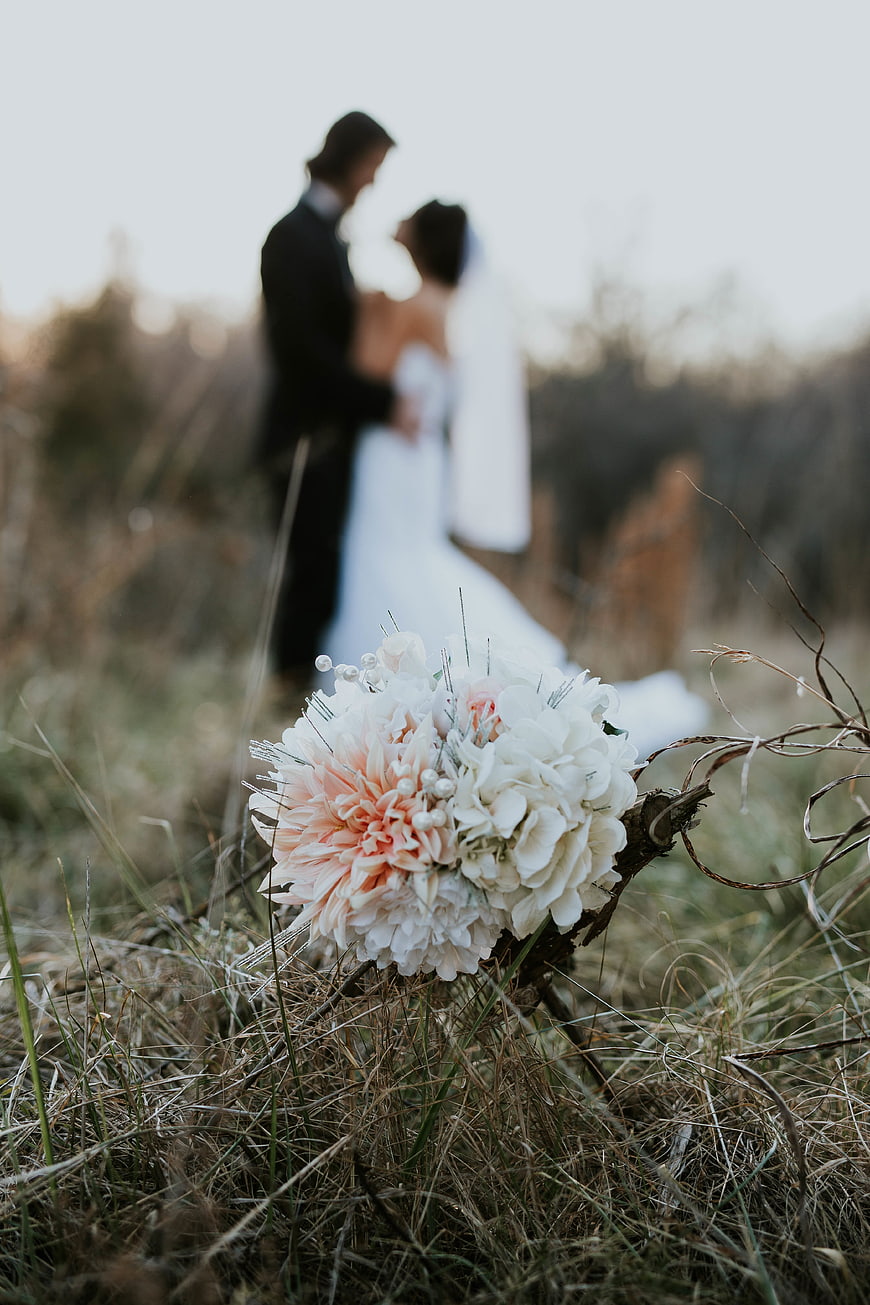 Wedding bouquet in grass with blurred couple background
