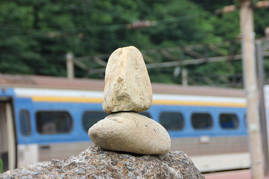 Balanced stone cairn on a rock with a blurred blue train in the background