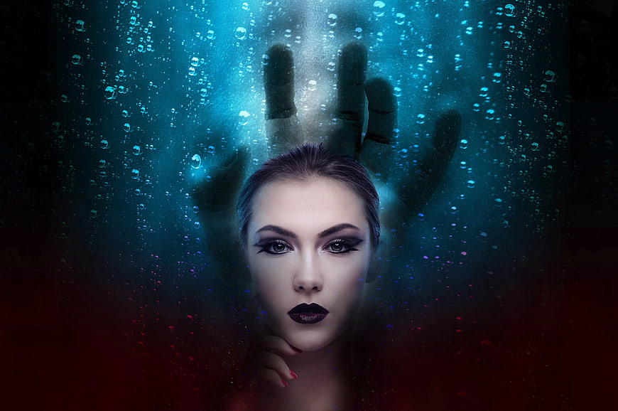 Woman with dark makeup behind glass with hand silhouette
