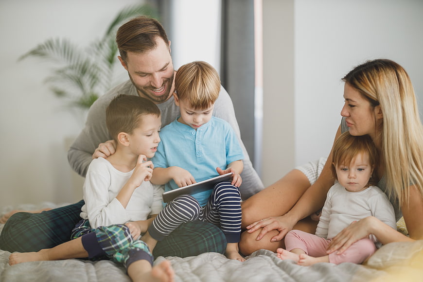Happy family with children using tablet on bed