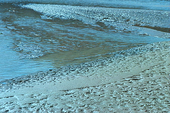 Close-up of wet sand texture and gentle ocean waves on a beach
