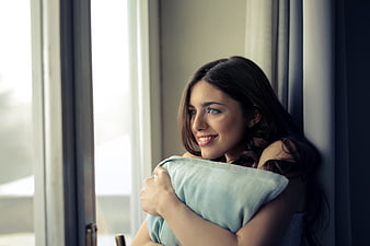 Happy Woman Smiling While Hugging Pillow by Window