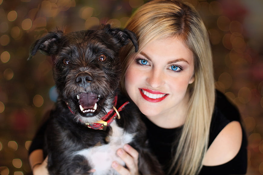 Happy Blonde Woman Holding Cute Black Dog with Christmas Lights