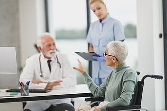 Senior female patient in wheelchair consulting with doctor and nurse