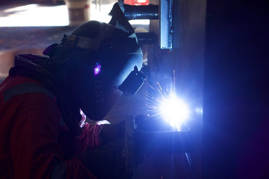 Industrial Welder Working With Bright Sparks In Dark Factory