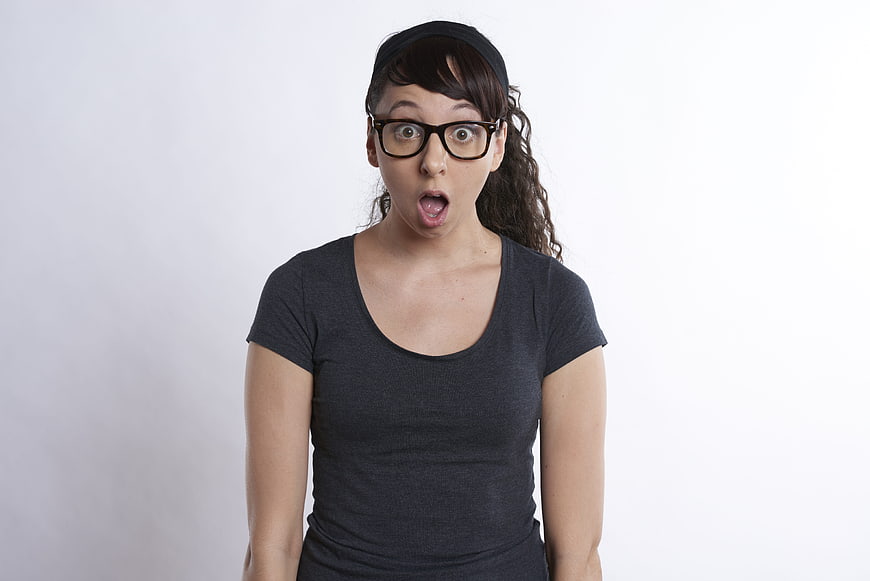 Surprised young woman with glasses and headband on white background
