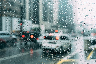 Raindrops on car windshield with blurred city traffic background