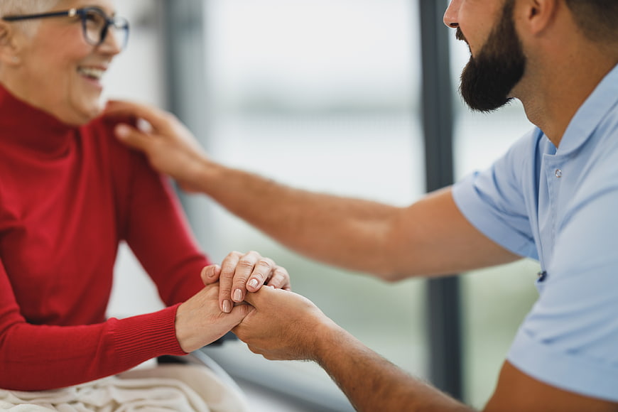 Male caregiver holding hands with smiling senior woman