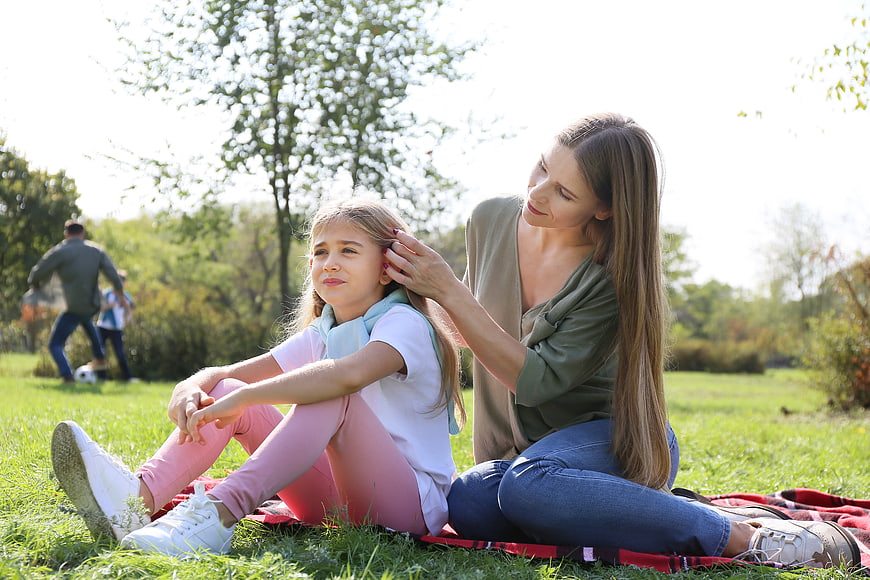Mother fixing daughter's hair in sunny park