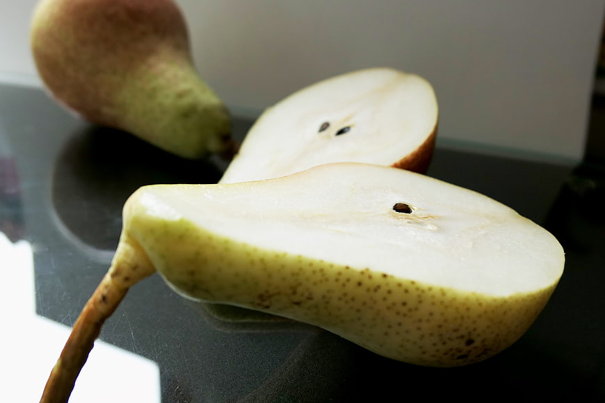 Fresh sliced pear on dark surface with whole fruit