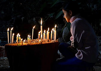 Woman praying at night with lit candles in dark outdoor setting
