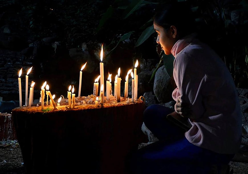 Woman praying at night with lit candles in dark outdoor setting