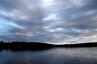 Dramatic Cloudy Sky Over Calm Lake with Tree Silhouette