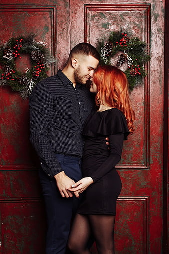 Romantic Young Couple Embracing in Front of Red Christmas Door