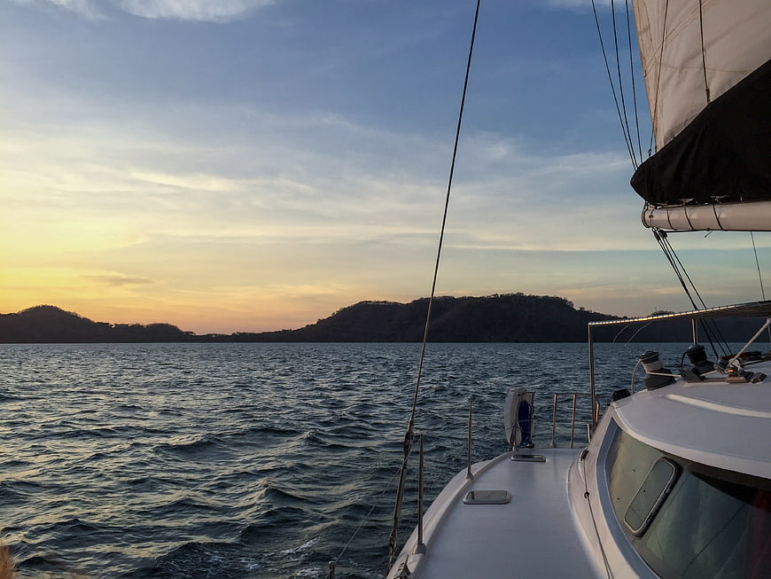 Sailboat bow sailing on ocean at sunset with distant hills