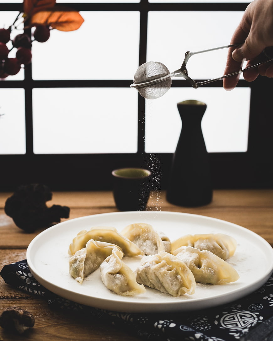 Hand Sifting Sugar Powder Over Steamed Dumplings on White Plate