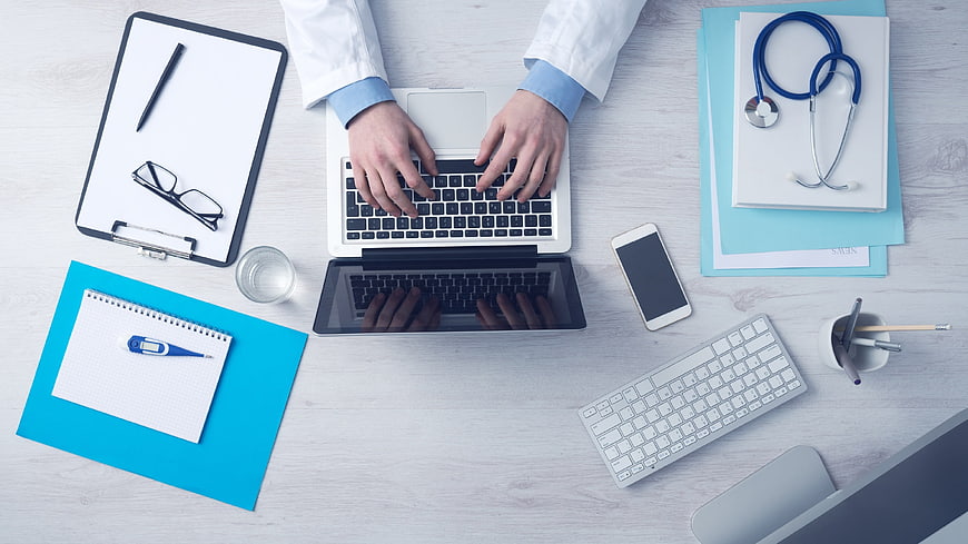 Doctor typing on laptop with stethoscope and medical tools