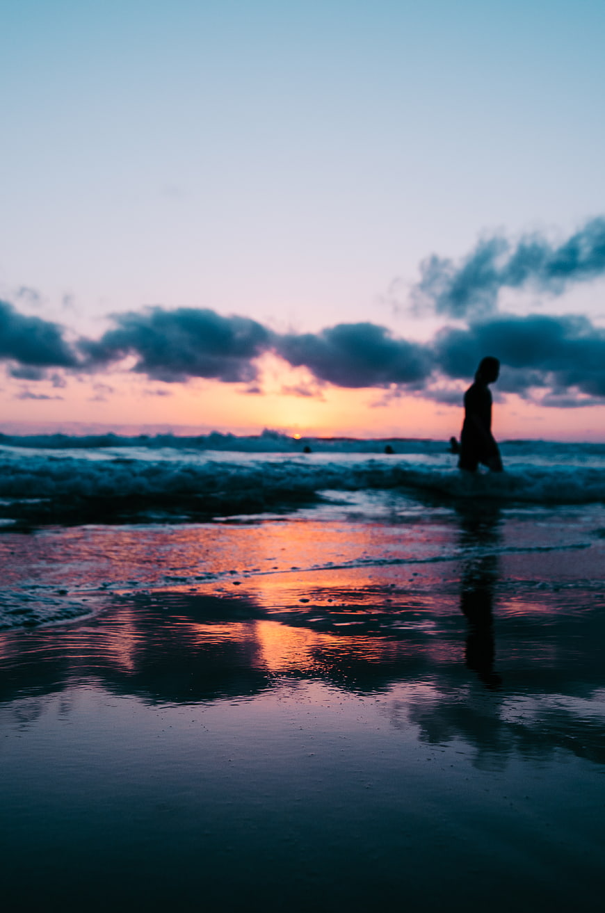 Silhouette of person walking on beach at sunset with reflection