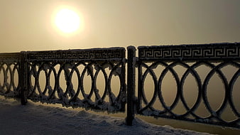 Frost-covered metal railing against a bright winter sunrise