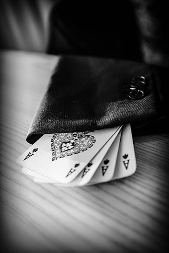 Four Aces of Spades fanned out from a black suit sleeve on a wooden table