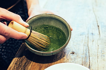 Hands whisking matcha green tea in ceramic bowl