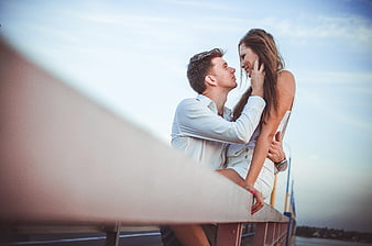 Romantic young couple embracing on a bridge railing at dusk