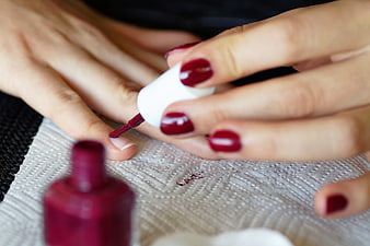Close-up of hands applying deep red nail polish on a textured towel
