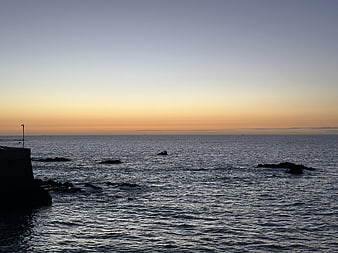 Serene Ocean Sunset with Silhouetted Rocks and Calm Waters