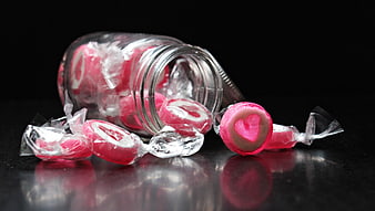 Pink heart candies spilling from glass jar on black background