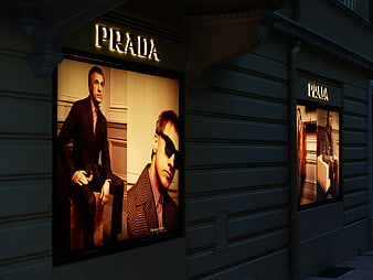 Illuminated Prada storefront with fashion advertising posters at night