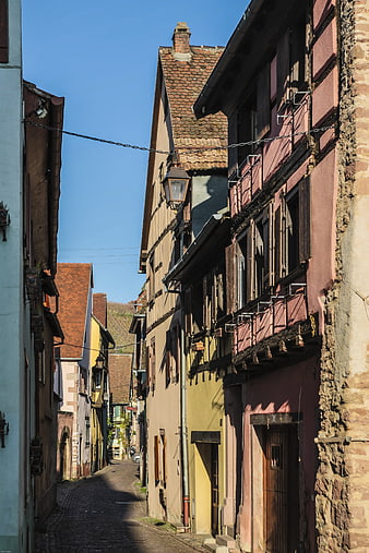 Narrow cobblestone alley in historic Alsace village with colorful half-timbered houses