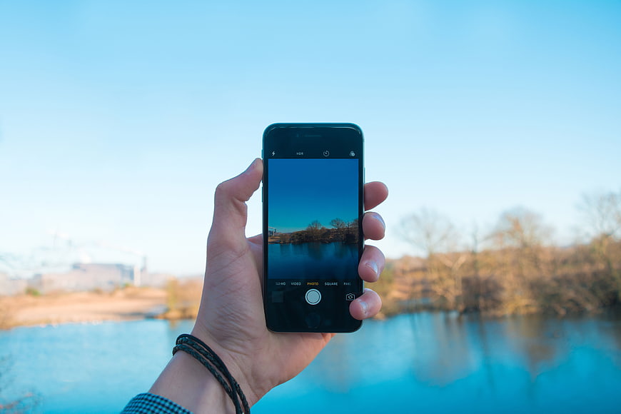 Hand holding smartphone taking photo of lake landscape
