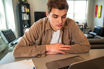 Young man looking concerned while working on laptop at desk