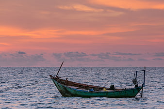 Traditional wooden fishing boat floating on calm ocean at sunset