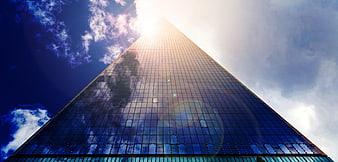 Low angle view of a modern glass skyscraper reaching toward the sun