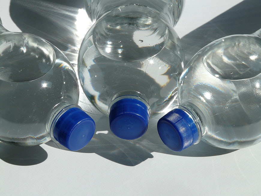 Three Clear Plastic Water Bottles With Blue Caps On White Surface